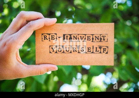 Femme main tenant la carte en carton avec des mots vous-même Re-Invent faites par contre timbres alphabet noir vert nature arrière-plan. Banque D'Images