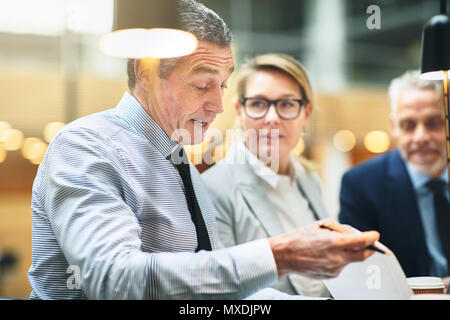 Mature businessman reading formalités administratives tout en ayant une réunion avec deux collègues à une table dans un bureau moderne Banque D'Images