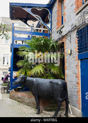 Statue d'une vache noire se tient à l'extérieur du marché de Pannier Truro avec un balcon bleu et Trachycarpus fortunei derrière palm Banque D'Images