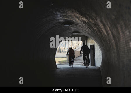 Les cyclistes en silhouette sortir rétroéclairé d'un tunnel d'une vieille ville Banque D'Images