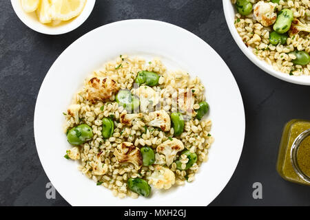 Des vegan salade faite d'orge perlé, des fèves, du chou-fleur rôti et le persil, vinaigrette et les tranches de citron sur le côté Banque D'Images