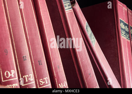 Une vieille collection encyclopédie rouge debout dans une étagère couvertes de poussière. Banque D'Images