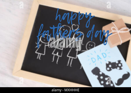 Les enfants s'appuyant sur un tableau noir avec carte de vœux et boîte-cadeau sur fond en bois. Concept de la fête des Pères Banque D'Images