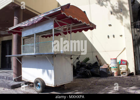 Panier alimentaire abandonnés enchaînés à un bâtiment abandonné. Sur le côté, noir sacs de détritus et des contenants vides. Banque D'Images