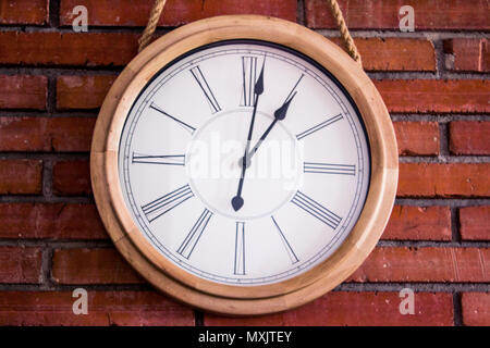 Close-up d'une horloge murale en bois avec chiffres romains suspendus dans un mur de brique rouge. Banque D'Images