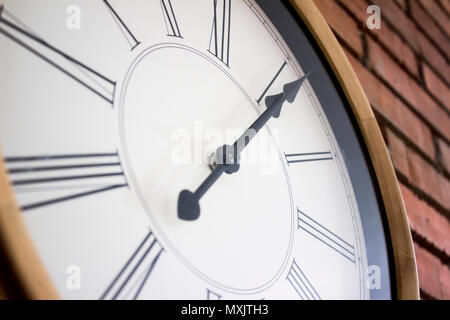 Side close-up d'une horloge murale en bois avec chiffres romains suspendus dans un mur de brique rouge. Banque D'Images