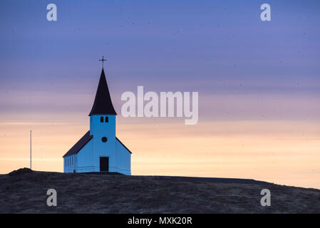 Pourpre et orange lever de soleil sur l'église Vik en Islande au sommet d'une colline, entouré de centaines d'oiseaux Banque D'Images