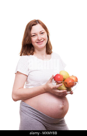 Femme enceinte en souriant à la caméra possède un bol en verre avec des fruits dans ses mains Banque D'Images