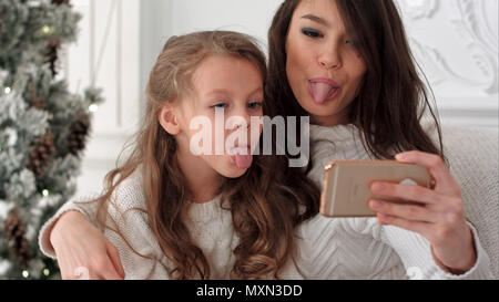 Cheerful young mother and her daughter making comic xmas autoportraits et montrant langues Banque D'Images