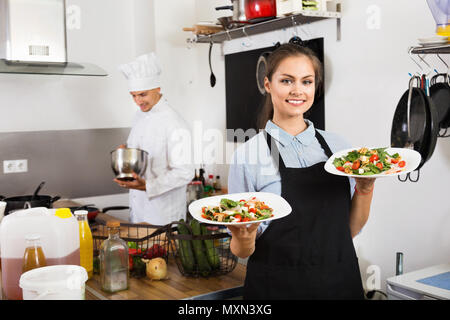 Portrait of young beautiful smiling woman wearing apron serveuse et tenant prêt à servir la salade Banque D'Images