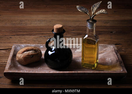 Un cadre rustique sur bois d'une miche de pain, un récipient de vinaigre balsamique, et une bouteille en verre d'huile d'olive. Banque D'Images