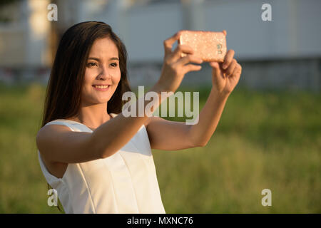 Young happy Asian woman smiling tout en tenant avec photo selfies Banque D'Images