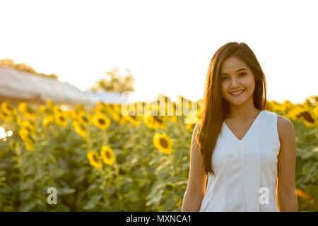 Young happy Asian woman smiling in le domaine de sunflow en fleurs Banque D'Images