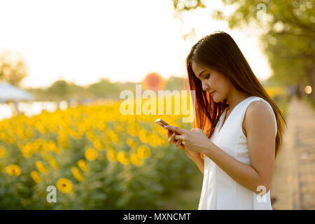 Belle jeune femme asiatique à l'aide de téléphone mobile contre un champ de Banque D'Images