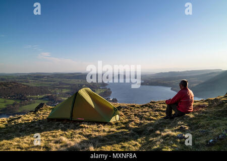 Middle-Aged Backpacker assis à l'extérieur de leur tente profiter tôt le matin Voir plus de Ullswater Hallin est tombé, Lake District, Cumbria, Royaume-Uni. Banque D'Images