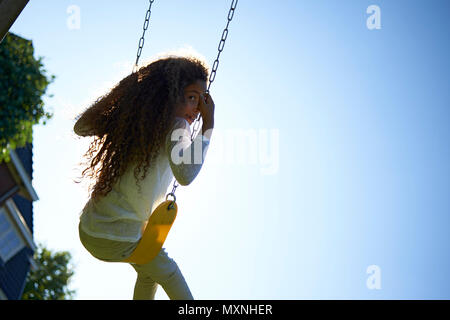 Un jeune preteen girl avec de grands cheveux bouclés assis dans l'herbe dans son jardin à l'arrière dans le soleil d'été à jouer avec une tablette pour surfer sur le web Banque D'Images