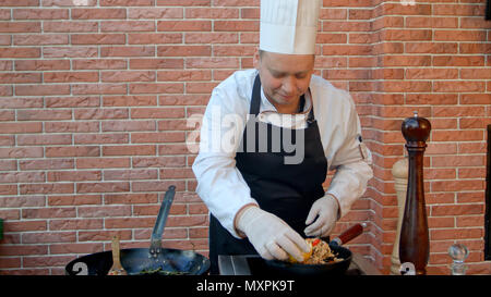 Beau male chef habillé en uniforme blanc décorant la paella et regardant la caméra smiling Banque D'Images