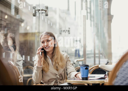 Vue de face d'une jeune femme d'adultes de passer un appel téléphonique et d'avoir un café avant de travailler. Banque D'Images