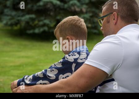 Père et fils : un père laisse son fils de 5 ans à diriger le tracteur-tondeuse qu'il coupe l'herbe Banque D'Images