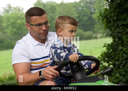 Père et fils : un père laisse son fils de 5 ans à diriger le tracteur-tondeuse qu'il coupe l'herbe Banque D'Images