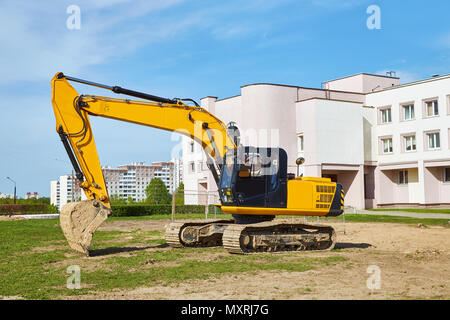 Une excavatrice jaune avec un taxi noir se dresse sur le terrain, dans l'arrière-plan des bâtiments résidentiels Banque D'Images