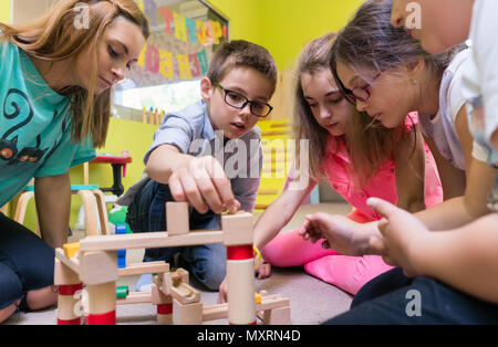 Enseignant de maternelle dédié à aider les enfants avec la construction d'un train Banque D'Images