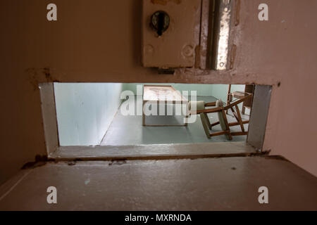 Cadre de lit en métal avec une chaise et un bureau à l'intérieur de l'isolement cellulaire par des cellules en lattes de porte en métal ancienne prison. Banque D'Images