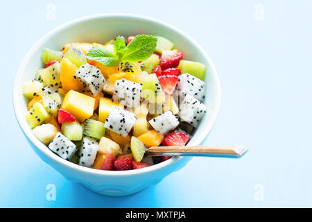 Salade de fruits exotiques et de mangue dans un bol de pitaya isolé sur fond bleu clair. L'espace de copie pour le texte. L'été, des vacances, une alimentation saine et un Banque D'Images