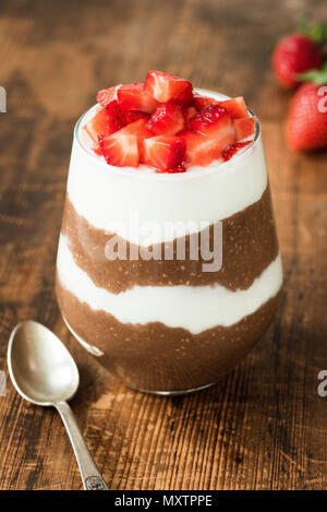 Chia pudding avec du yaourt, chocolat et fraises dans un verre sur la table en bois. Vue rapprochée, selective focus Banque D'Images