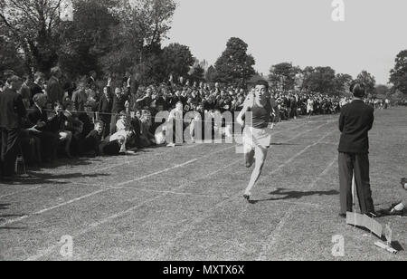 1960, tableau historique de l'écolier secondaire qui participent à une course à pied à un comté inter-écoles sports le jour, Dorset, England, UK. Nous voyons ici le gagnant le sprint pour traverser la bande de finition en face d'une foule d'autres élèves à côté de la piste. Banque D'Images