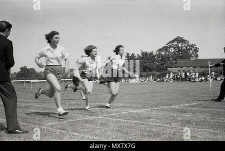 1960, tableau historique des écolières secondaire qui participent à une course à pied, les 100 verges dans un comté inter-écoles sports le jour, Dorset, England, UK. Nous voyons ici trois des filles sprintant pour la bande de finition. Banque D'Images