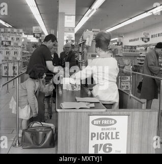 Années 1960, historique, le père avec sa jeune fille aidant avec leurs propres sacs de shopping à la caisse d'à un nouveau type de magasin de détail, un magasin libre-service, appelé', les romans en Angleterre, Royaume-Uni. C'est après la disparition de rations alimentaires en 1954 lorsque la consommation du personnel a commencé à se développer et dans les années 60 les supermarchés tels que nous les connaissons aujourd'hui a vraiment commencé à se développer dans le Royaume-Uni, bien qu'un grand nombre de marques d'origine ont été repris ou ont fusionné avec d'autres chaînes. Banque D'Images