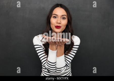 Heureux jolie brunette woman in sweater envoie baiser de l'air en regardant la caméra sur fond noir Banque D'Images