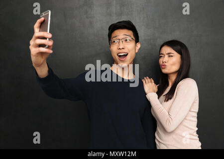 Happy asian couple posing together et décisions sur smartphone selfies sur fond noir Banque D'Images