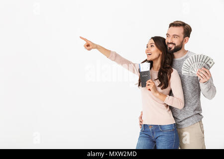 Photo de heureux jeune couple aimant isolés sur fond blanc holding passport et billets pointant à côté. Banque D'Images