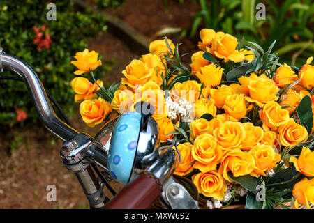 Vieux vélo stationné dans un parc avec des fleurs artificielles jaunes dans votre panier Banque D'Images