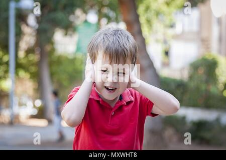 Stressé peu 5-ans caucasien petit garçon en dehors de fermer ses oreilles et des hurlements de douleur, traumatisme, l'expérience traumatique et bruit important stock Banque D'Images