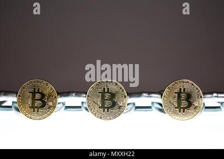 Trois des Bitcoins est situé sur une surface brillante blanc tandis qu'une chaîne en métal acier lourd se trouve derrière. Concepts de la technologie de la chaîne d'bloc et la monnaie numérique. Banque D'Images