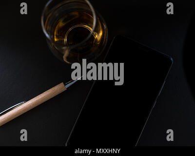 Stylo en bois avec verre de whisky et le smartphone à partir de ci-dessus, surface sombre Banque D'Images