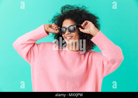 Fashion portrait de femme élégante 20s avec coiffure afro souriant et portant des lunettes de soleil moderne noir isolé sur fond bleu Banque D'Images