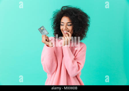 Portrait de femme de charme 20s avec coiffure afro détenant une carte de crédit en plastique avec plaisir isolé sur fond bleu Banque D'Images