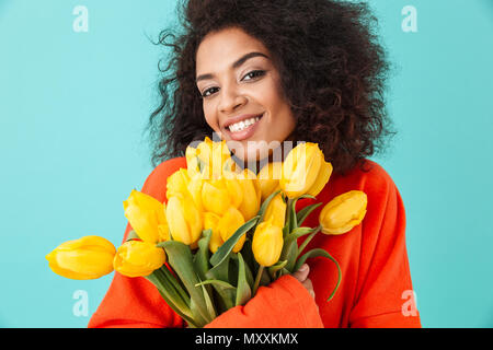 Femme magnifique avec des cheveux en désordre à la recherche sur la caméra et holding bouquet de belles fleurs jaune isolé sur fond bleu Banque D'Images