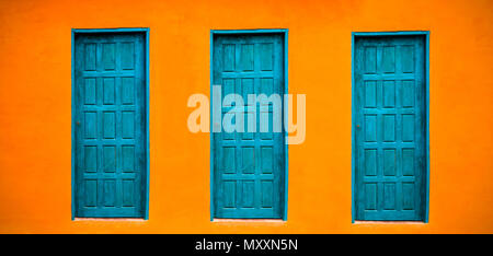 Orange vif vif wall façade de maison avec trois portes fermées bleu-vert sur le grand mur vide large orange texture background space dans panorama banner f Banque D'Images