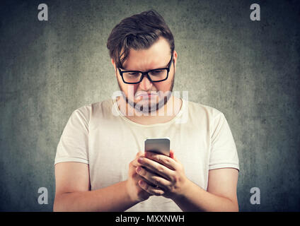 Jeune homme triste occasionnels reçu message offensant sur smartphone à la colère et sombre Banque D'Images