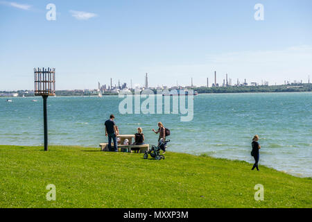 Les gens qui profitent du soleil à Netley Beach le long de Southampton Water avec la raffinerie Fawley en arrière-plan Mai 2018, Netley, Hampshire, Angleterre, Royaume-Uni Banque D'Images