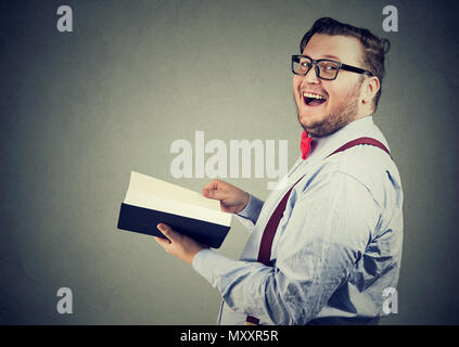 Vue latérale d'heureux chubby man reading livre intéressant et rire à huis clos sur fond gris Banque D'Images