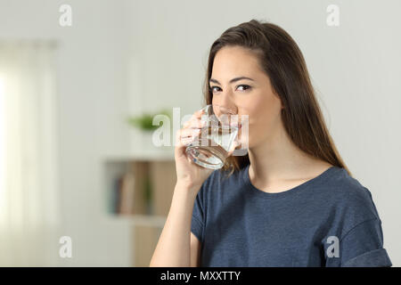 Femme de l'eau potable dans un verre transparent et vous regarde à la maison Banque D'Images