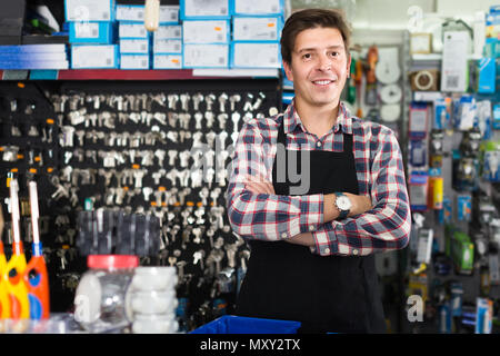 Cheerful worker in hardware store commerce des marchandises pour un robinet d'eau en uniforme Banque D'Images