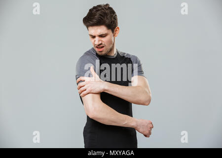 Portrait of a bouleversé les jeunes sportifs souffrant d'une douleur à l'épaule sur fond gris isolé Banque D'Images