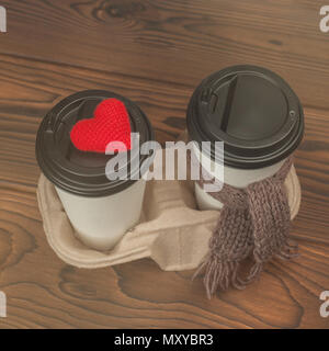 Paire de tasses à café à emporter blanc avec couvercle noir et fond de bois, tricotez cœur rouge et foulard Banque D'Images